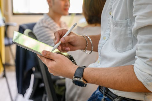 Nahaufnahme einer Person, die in einer modernen Büroumgebung mit einem Stylus auf einem iPad schreibt.